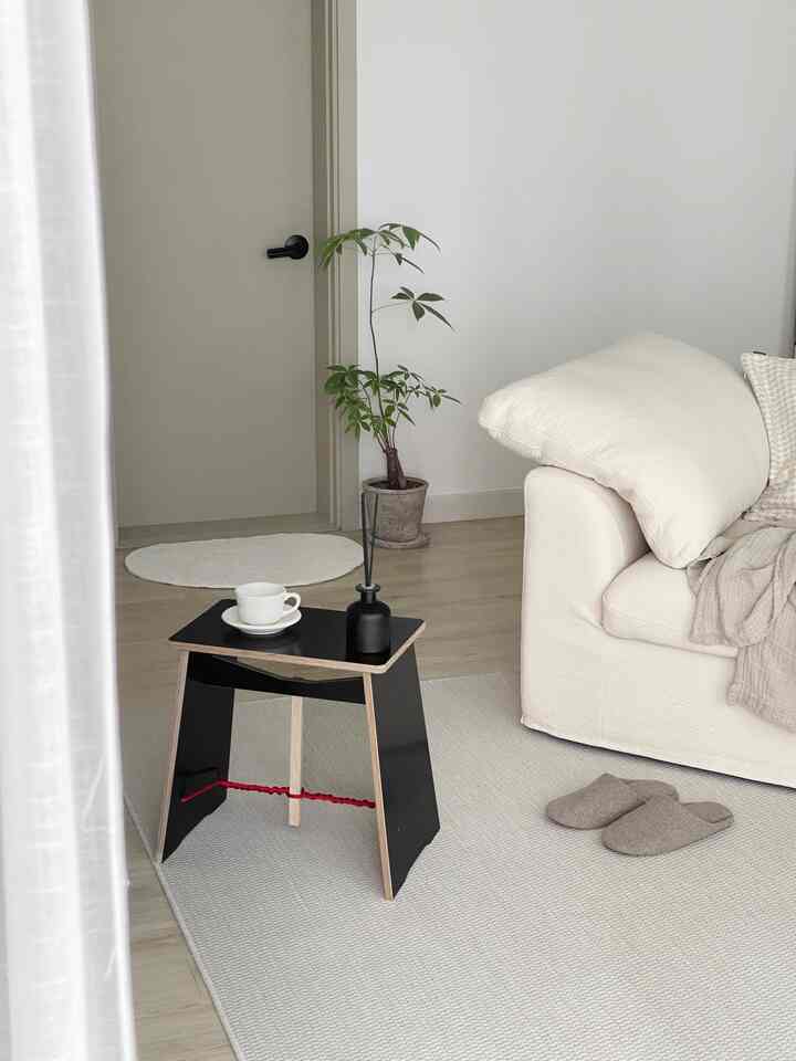 ナチュラルで明るい色調のリビング、白いソファと黒いスツール、コーヒーカップとディフューザーが置かれた温かみのある空間