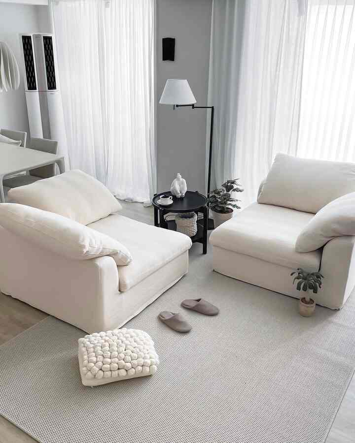 明るいホワイトトーンのリビング、クリーム色のモジュラーソファ2つとサイザル風ラグ、フロアランプが配置されたシンプルで自然な雰囲気のインテリア