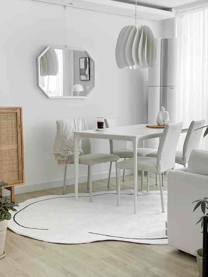 明るいホワイトトーンとウッド調が調和したダイニングルーム、白いダイニングテーブルと椅子、ペンダントライト、カーテン、個性的なラグが配置されたシンプルなインテリア