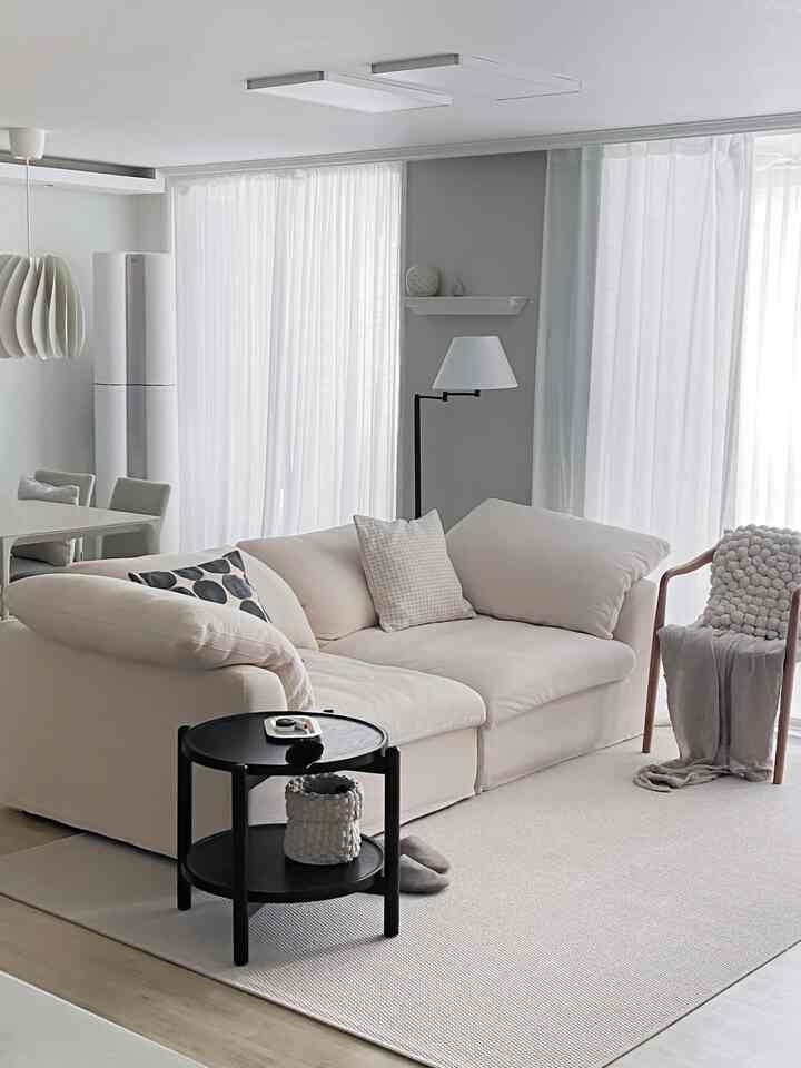 白とベージュの色調のリビング、ファブリックソファと黒のサイドテーブル、フロアランプが配置されたシンプルでナチュラルなインテリア