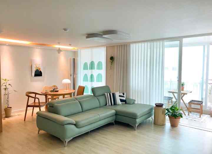 ナチュラルカラーと木目調が調和したリビング、グリーンのレザーソファと丸いダイニングテーブルが置かれた明るく落ち着いた雰囲気のインテリア