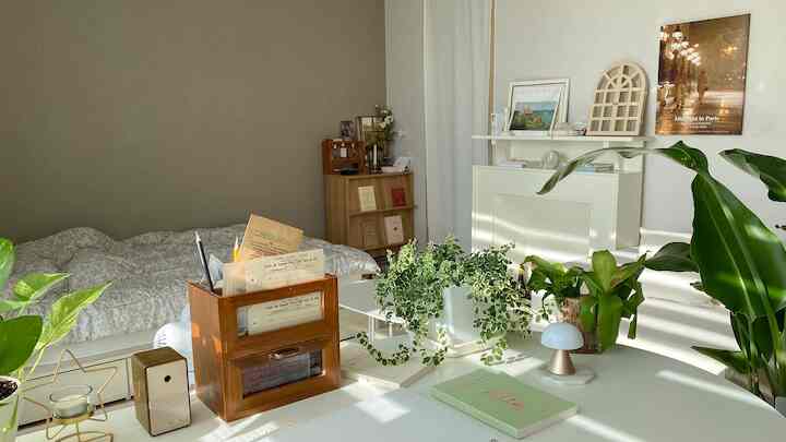 ホワイトとナチュラルトーンの寝室、植物と小さな家具が配置された自然光あふれる印象的な空間