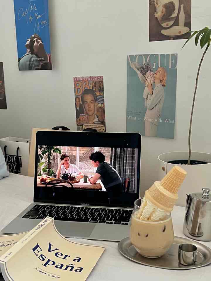 白い壁とポスターが配置されたおうちカフェの空間、中央にノートパソコンと銀色のトレイにのったアイスラテがある雰囲気のあるインテリア