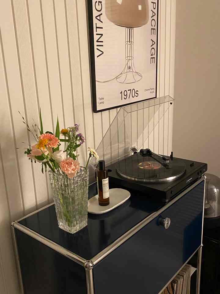 ブルー色調のUSM収納の上にターンテーブルと造花の花束が置かれた寝室のコーナーインテリア