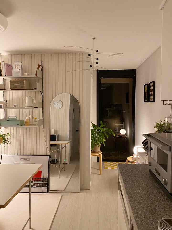 ホワイトとベージュの落ち着いたキッチン兼玄関スペース、モビールと植物がポイントのミニマルなインテリア