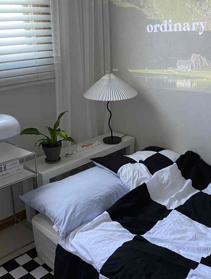 白と黒のトーンが印象的な寝室、チェック柄の掛け布団カバーと快適な寝具が配置されたモダンで清潔感のあるインテリア