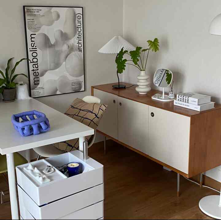 白と木目調のリビング、モダンでシンプルなデスクとサイドボード、植物と照明が配置された清潔感あるインテリア