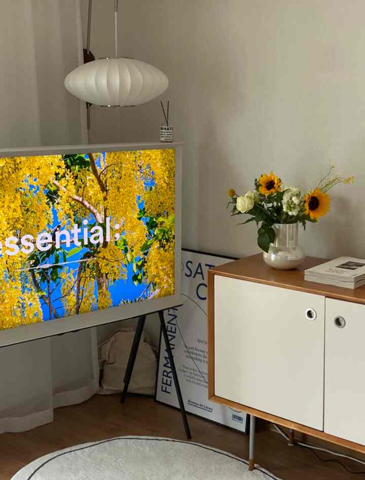 ホワイトと木目調のリビング、サムスン セリフ テレビとキャビネット、ヒマワリの花瓶が配置されたシンプルでモダンな空間