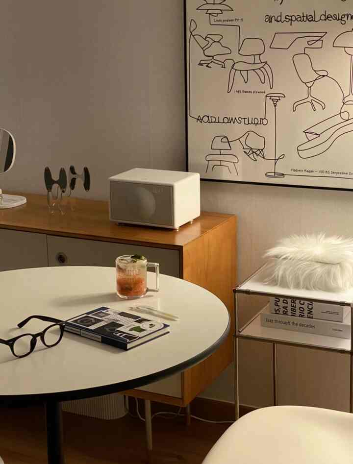 ナチュラルな木目調とホワイトトーンのリビング、丸いコーヒーテーブルとBluetoothスピーカー、額装ポスターが置かれた落ち着いた空間