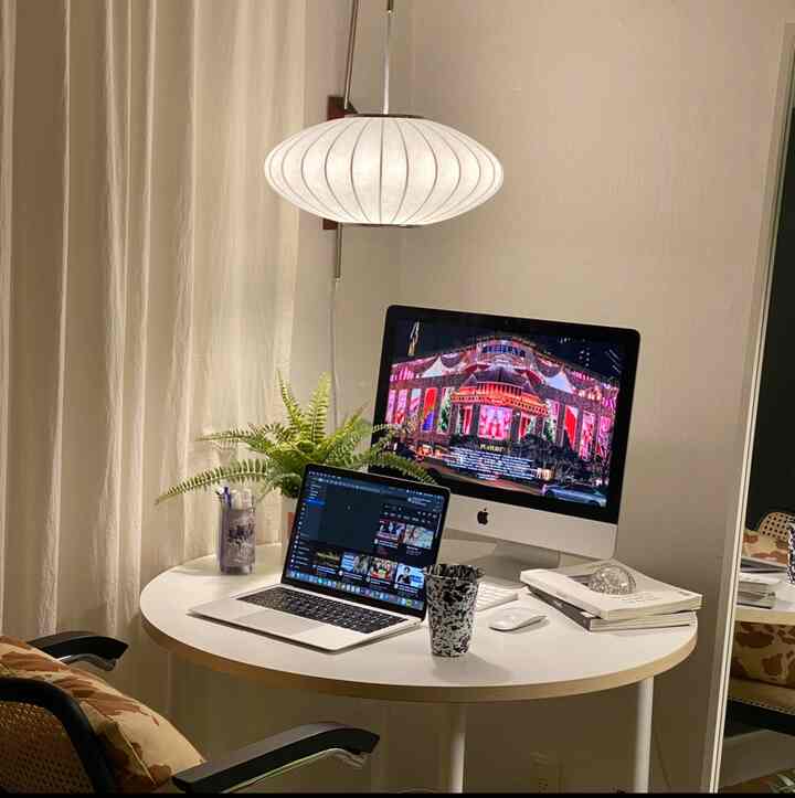 白とアイボリーのトーンのホームオフィス、丸テーブルにモニターとノートパソコン、植物が配置された清潔感のある作業空間