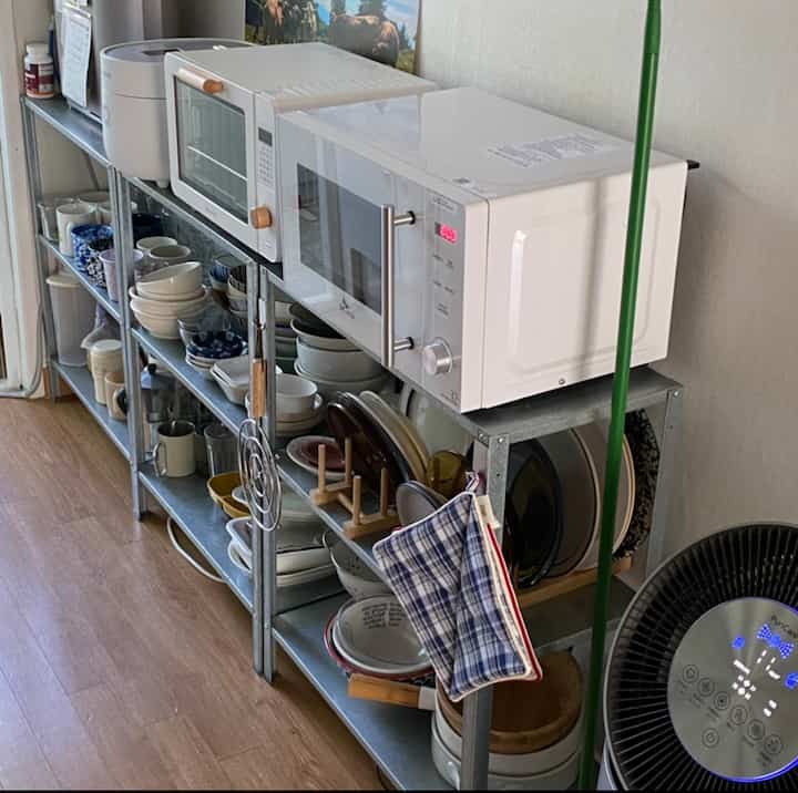 白を基調としたキッチン、金属製棚に設置された電子レンジとオーブン、多様な食器が整頓された印象的な空間