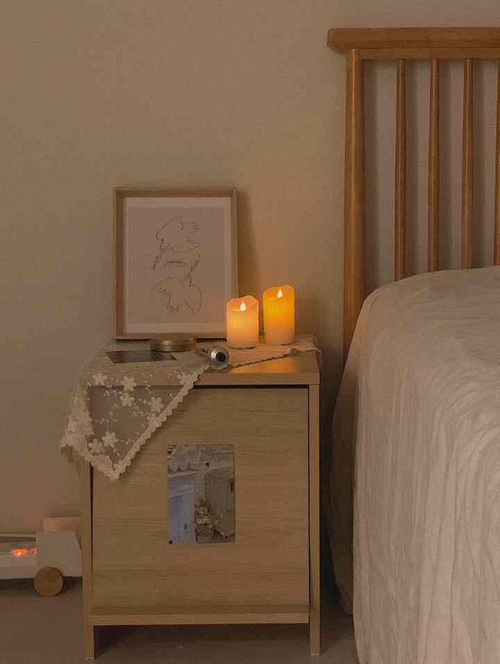 ナチュラルな木目調とベージュ色調の寝室、ナイトテーブルとベッドが配置され、温かみのあるキャンドル照明が印象的な空間