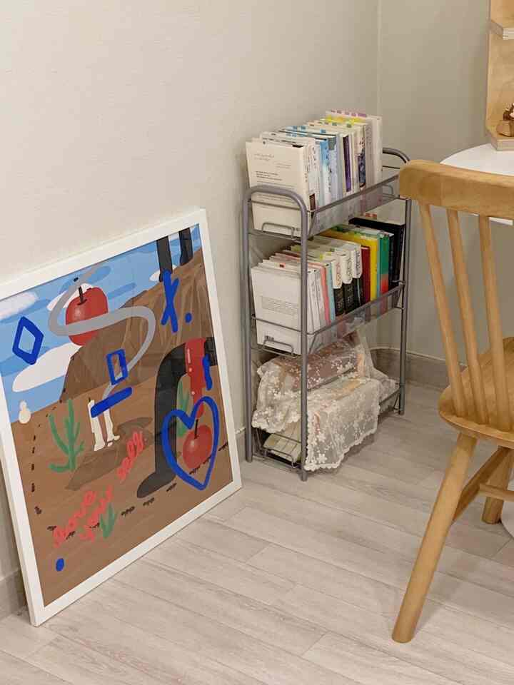 ナチュラルな木目調と白い壁のコンパクトな空間に、コーナーに本が整頓されたメタル収納ラックが置かれた印象的なインテリア