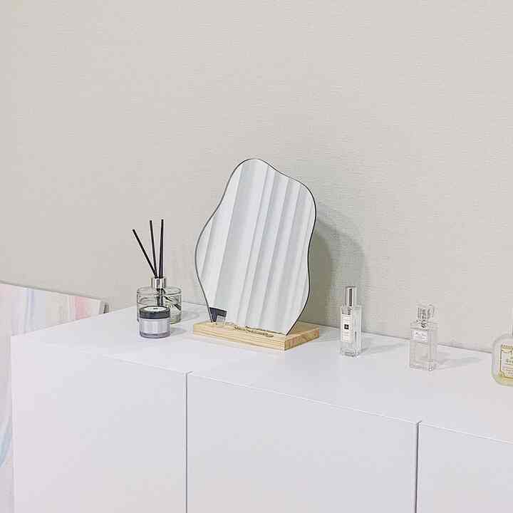 白い壁と収納が調和した空間に、抽象的な形の鏡とディフューザーが置かれたシンプルで清潔感のあるインテリア