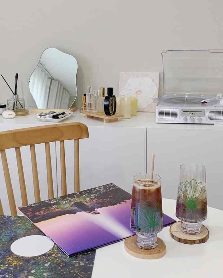 白とナチュラルカラーの寝室、木製チェアと白いテーブル、LEDキャンドルとLPターンテーブルが配置されたシンプルなインテリア