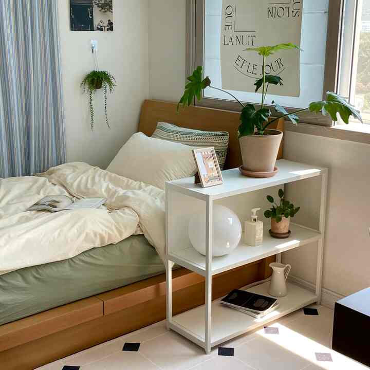 ナチュラルな色調と白を基調とした寝室、木製ベッドと植物、すっきりとした棚が配置された雰囲気のあるインテリア