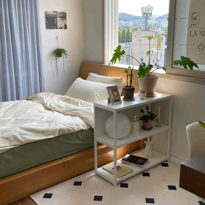 白と木目調が調和した温かみのある寝室、ベッドと棚に植物が置かれ、自然光が差し込む雰囲気のあるインテリア。