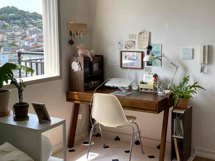 白い壁と木目調家具が調和した6畳のホームオフィス、植物とノートパソコンスタンドが配置された落ち着いた作業空間