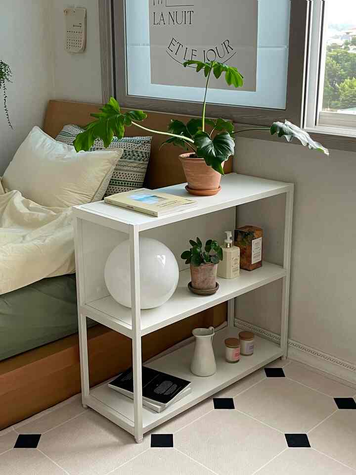 ホワイトの鉄製本棚と木製スタンドが調和したナチュラルな寝室、植物や本が配置され、落ち着いた雰囲気のインテリア