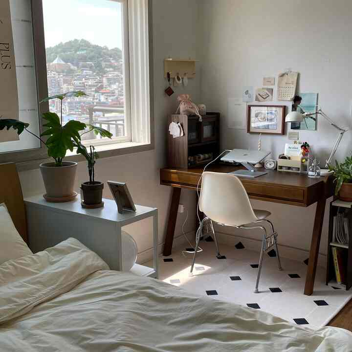 ホワイトとブラウンの色調の寝室、木製デスクと白い椅子、ラグが配置された居心地よくシンプルなホームオフィス空間