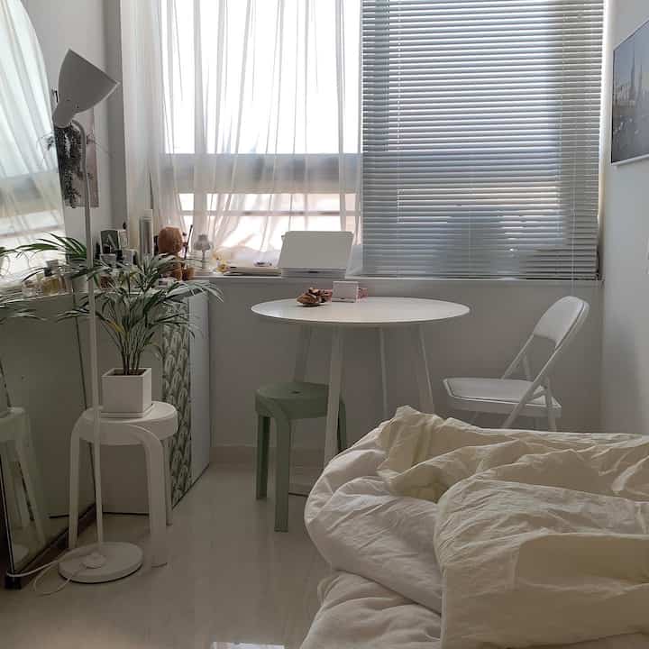 白とベージュの色調のワンルーム、シンプルな丸テーブルと椅子、シフォンカーテンが配置された雰囲気のある小さな部屋