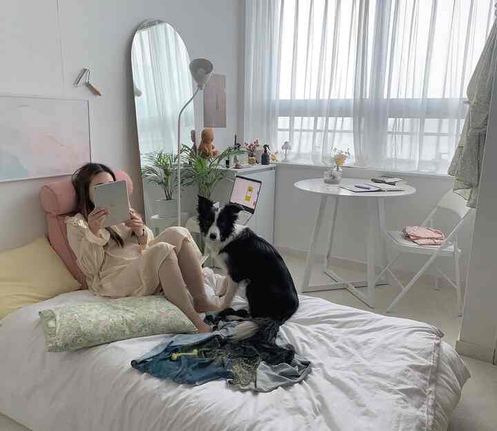 明るいホワイトトーンの寝室、中央にベッドと黒白の犬、左側に全身鏡とフロアランプが配置された印象的なインテリア