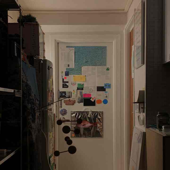 白を基調とした狭い玄関、入口の扉に様々なポスターやメモが貼られた空間