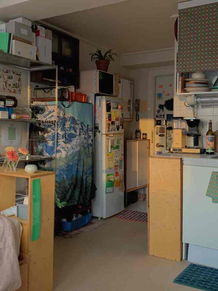 暖かいナチュラルカラーのワンルーム、キッチンとデスクが配置された雰囲気のある小さな居住空間