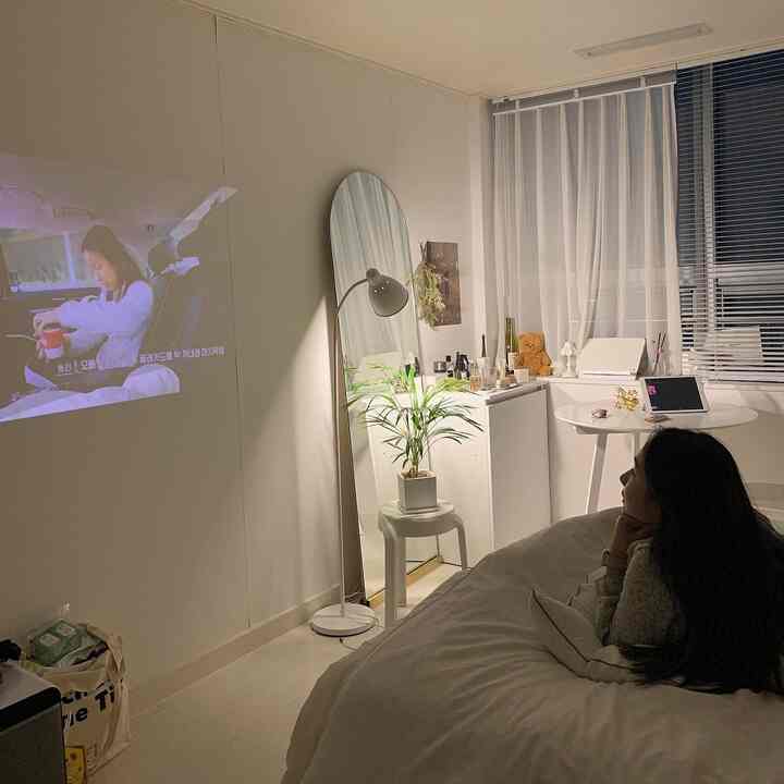 ホワイトトーンの寝室、プロジェクタースクリーンとアーチ型の鏡、フロアランプが配置された印象的な空間