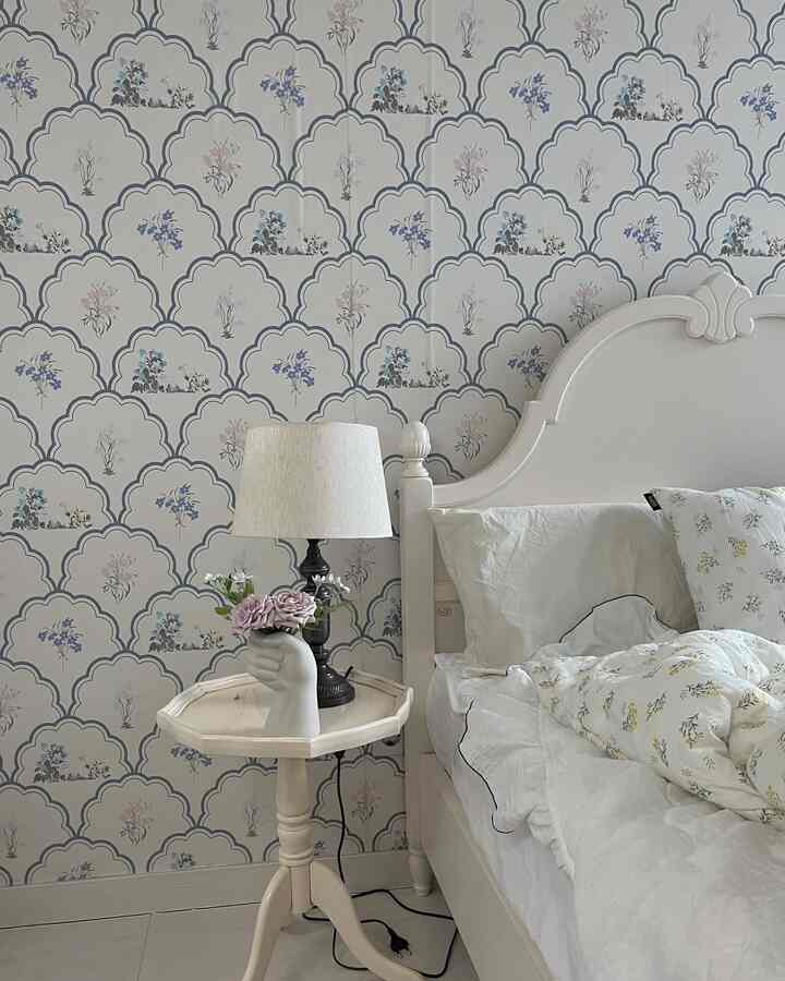 ホワイトトーンの寝室、フレンチカントリースタイルのベッドとナイトテーブル、手の形の花瓶とランプが配置された雰囲気のある空間