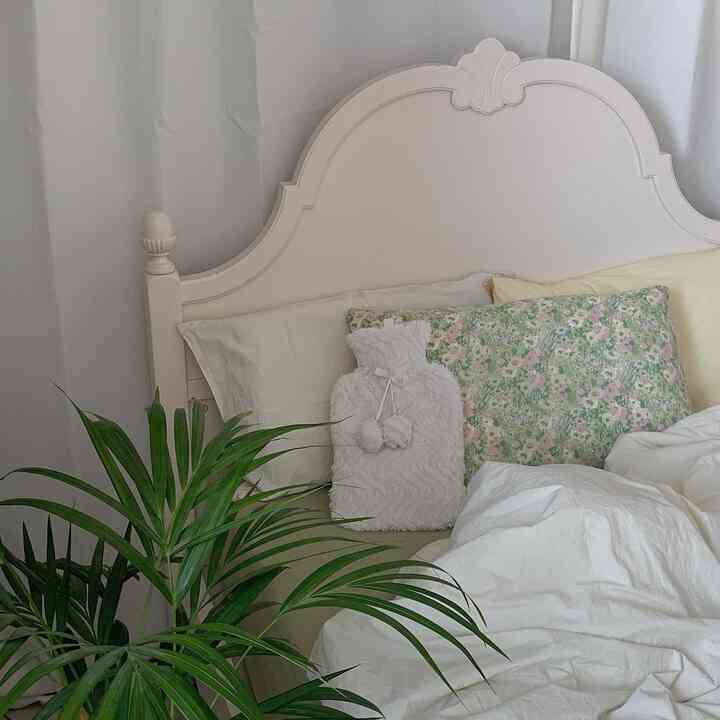 柔らかなホワイトトーンの寝室、装飾が施されたベッドフレームとカラフルな枕、緑の植物が調和した雰囲気のあるインテリア