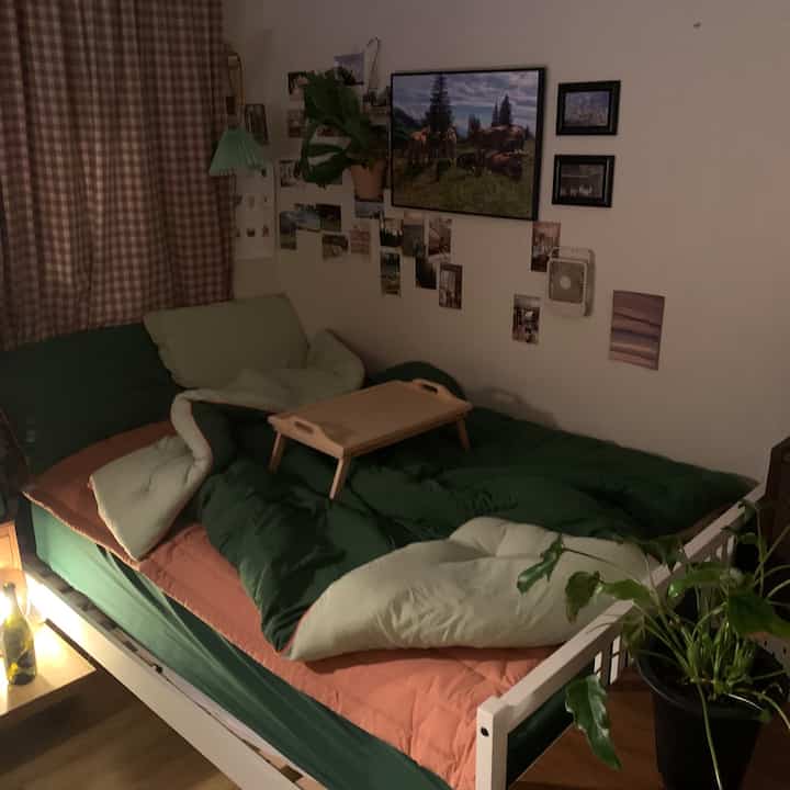 緑とベージュの自然な色調の寝室、ベッド、ベッドトレイ、壁飾りが配置された雰囲気のあるインテリア