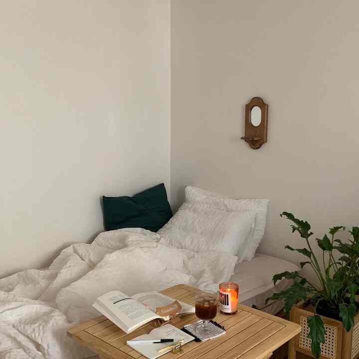 白とナチュラルカラーの寝室、ベッドと木製テーブル、観葉植物が配置された雰囲気の良い空間