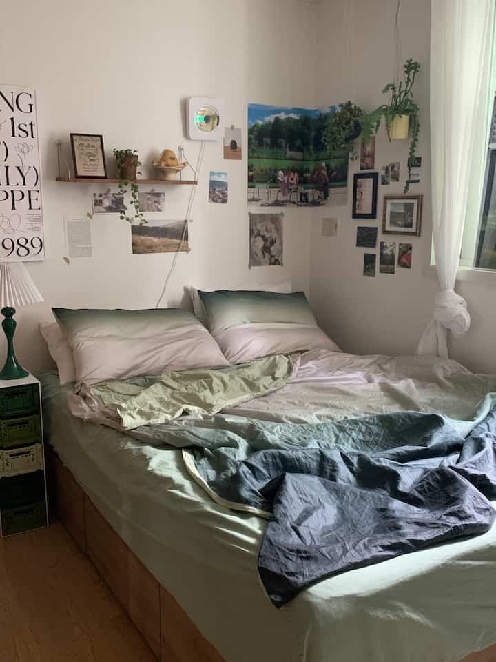 ナチュラルなベージュの壁とグリーンの寝具が配置された落ち着いた寝室のインテリア