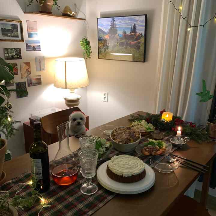 白い壁と木目調のダイニングルーム、クリスマスのホームパーティのために食事とキャンドルが並べられたテーブルと犬がいる温かみのある空間