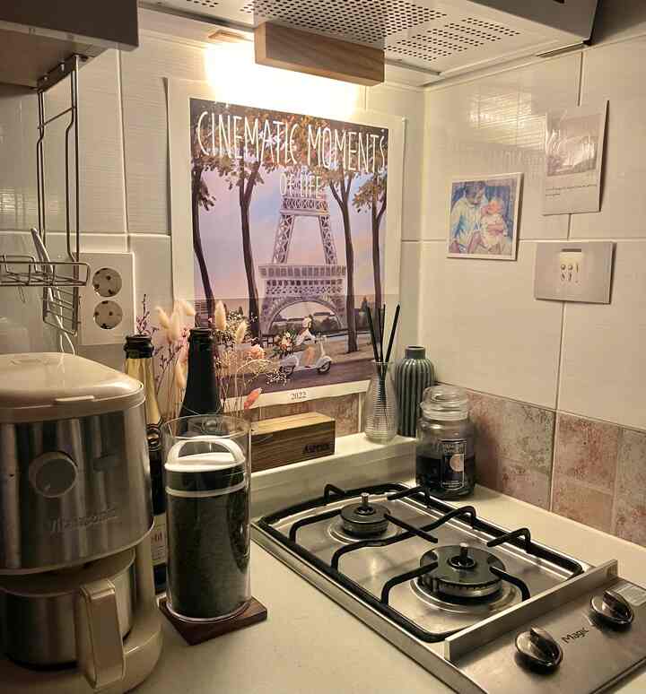 ホワイトとブラウンの色調のキッチン、カウンターと壁にコーヒーメーカー、キャンドル、ポスターが整然と配置された雰囲気のある空間