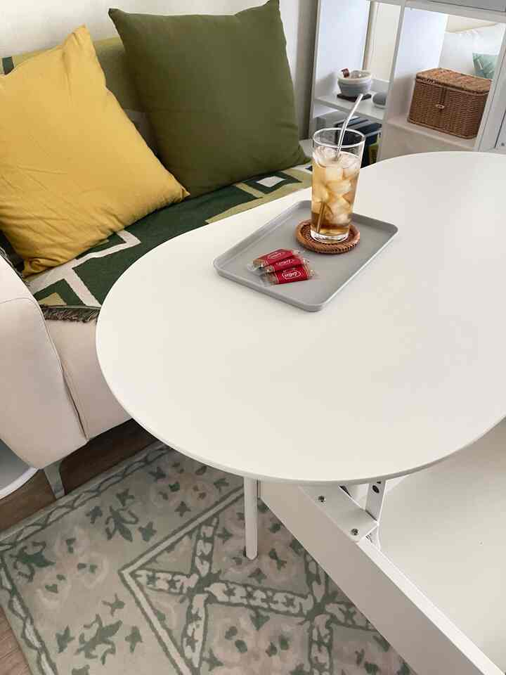 白と緑のトーンのリビング、リフトアップテーブルと幾何学的パターンのソファカバーが配置されたミニマルなインテリア