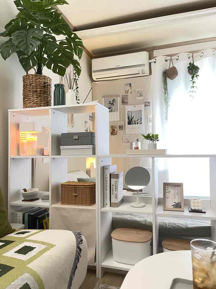 白と木目調のワンルームリビング、開放的な本棚と収納ボックスが配置された雰囲気のあるインテリア