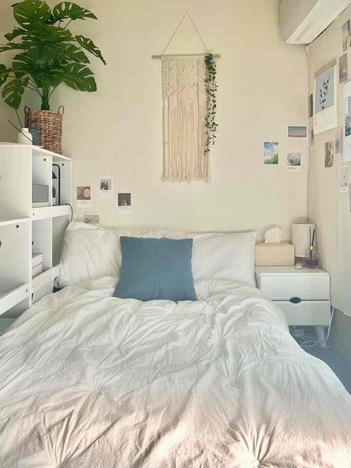 白とナチュラルカラーの寝室、中央にベッドと本棚、居心地の良い植物の装飾が配置された空間