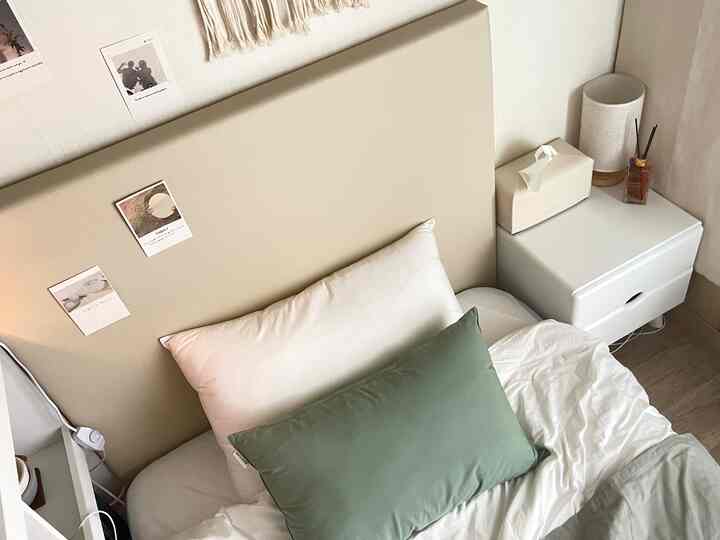 ベージュのヘッドボードと白いベッドリネンが配置された居心地の良い寝室、右側に白いナイトテーブルと間接照明を配した自然な雰囲気のインテリア