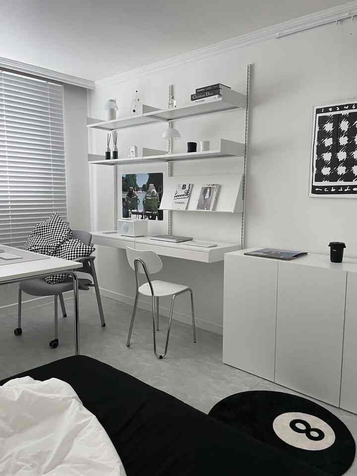 ホワイトとブラックのモノトーン寝室、ミニマルなホームオフィスセットアップに壁掛けデスクとエイトボールラグが配置された洗練された空間