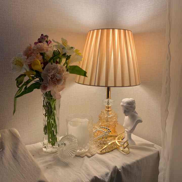 暖かいゴールド調とナチュラルなリネンの背景に、花瓶、石膏像、テーブルランプが調和したシンプルなインテリア空間