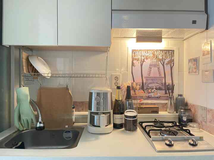 白とナチュラルトーンが調和したコンパクトなキッチン、コーヒーメーカーやワイン瓶、キャンドルが配置された清潔で温かみのある空間