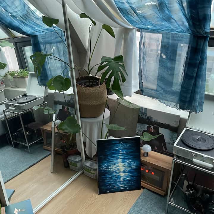 青とナチュラルトーンのカーテンがあるワンルーム空間、大きな観葉植物とヴィンテージターンテーブルが配置された雰囲気のあるインテリア