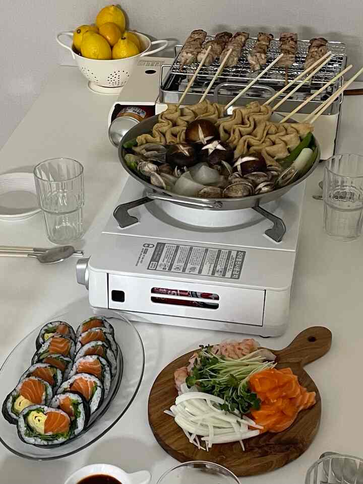 白と透明の色調が特徴的なダイニング、ホームパーティーのテーブルに鍋と串焼き、透明な皿が配置された雰囲気のあるインテリア