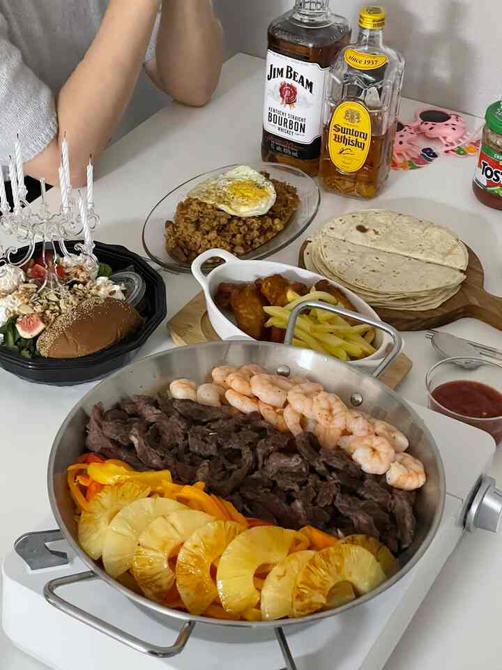 白いテーブルの上に様々な料理やバーナー、ソースボウルが配置されたホームパーティーの温かみのあるキッチン空間