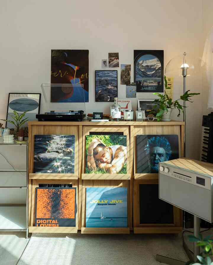 木目調の収納キャビネットとポスターが並ぶナチュラルなリビング、フロアランプとレコードプレーヤーが配置された雰囲気あるインテリア