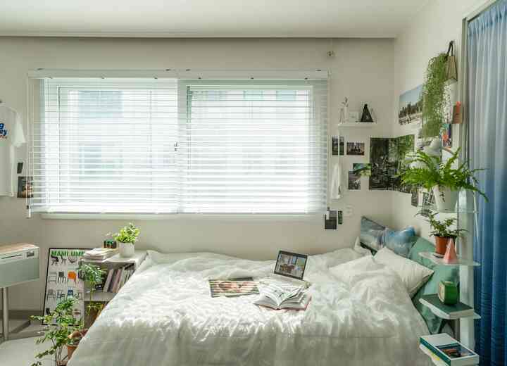 白と緑のトーンの寝室、中央に白いベッドと窓に設置された白いウッドブラインドが快適な雰囲気を演出しているインテリア