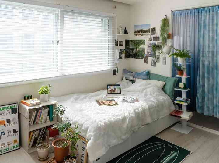 白と緑のトーンの寝室、ベッド中央に読書用の本とデジタル機器が置かれた自然で落ち着いた印象的なインテリア