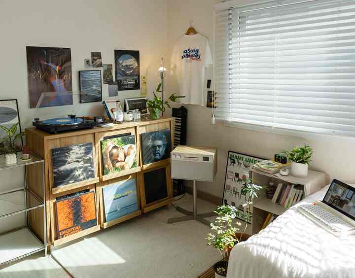 暖かい木目調の小さな音楽鑑賞スペース、木製収納ラックにLP、ターンテーブル、スピーカー、明るいラグ、植物が配置された雰囲気のあるインテリア